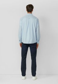 Chemise bleu clair à boutons avec manches longues, pli au dos et ourlet droit, associée à un jean foncé et des baskets blanches.