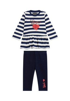 Gestreifte marineblaue und weiße Peplum-Bluse mit korallfarbenem Herz-Detail, kombiniert mit einfarbigen marineblauen Leggings, die auf dem Bein mit corallefarbenem "Guess"-Schriftzug versehen sind.