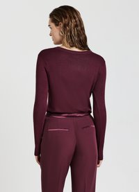 Burgunderfarbener Pullover mit langen Ärmeln und Rundhalsausschnitt, feiner Strickstruktur und passenden glatten Stoffhosen mit zwei Gesäßtaschen und einem Satinbund.