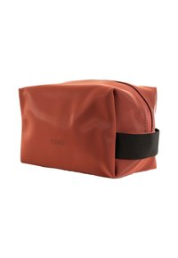 Neceser rectangular de color óxido, impermeable, con un asa de tela negra y cremallera en la parte superior, con la marca "RAINS" en un lateral.