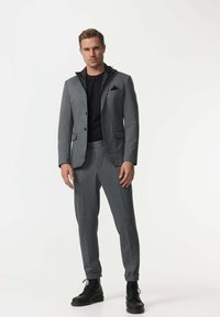 Grau maßgeschneiderter Anzug mit Kapuzenjacke, schwarzem Hemd darunter und passenden grauen Hosen. Texturiertes Material, elegantes Design, legere Stilelemente.
