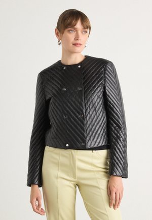 Gequilted zwarte leren jas met een ronde halslijn, zilveren drukknoopjes en lange mouwen, gecombineerd met lichtgele broek.
