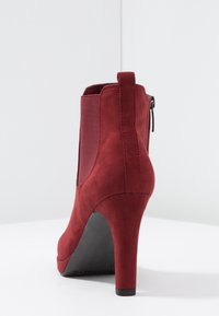Red suede ankle boot with a high heel, elastic side panels, and a back zipper. Smooth texture with a rounded toe and solid black sole.