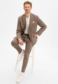 Bruin geruit pak met een getailleerde pasvorm, gecombineerd met een wit shirt en crèmekleurige sneakers. Opvallende kenmerken zijn een pochet en een gestructureerde stof.
