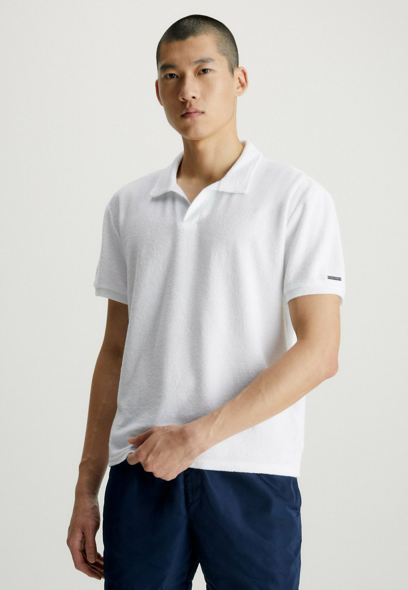 Polo shirt bianco a maniche corte realizzato in tessuto testurizzato, dotato di un colletto classico e di un piccolo logo sul maniche.