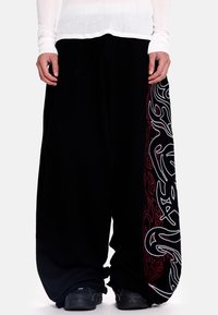 Juodos laisvos kelnės su plačiomis kojų dalimis. Kairėje pusėje yra sudėtingi balti ir raudoni liepsnos raštai. Pagamintos iš minkštos medžiagos.