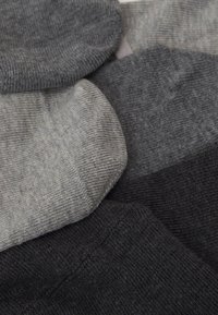 Fünf Paar Socken in verschiedenen Grautönen, mit gerippter Textur und runden Bündchen, übereinander auf einer flachen Oberfläche angeordnet.
