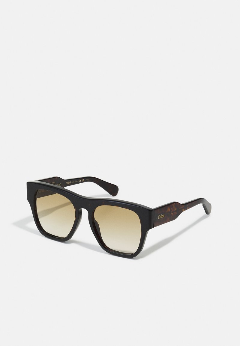 Oversized sunglasses with a black and tortoiseshell frame, gradient brown lenses, and gold "Chloé" logo on the arm. Flat design and angular shape.