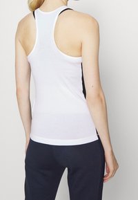 Vit linne med racerback-design; har svarta sidopaneler; tillverkat av mjukt, elastiskt material; slät textur, figurnära passform.