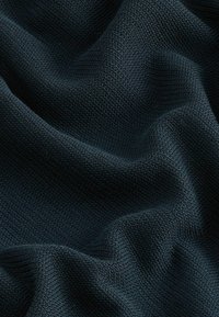 Struktureret mørkeblå stof med et strikket mønster, der viser bløde folder og en glat overflade, hvor lyset reflekteres fra fibre.