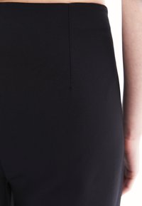 Svart stretchbyxa i tyg med en mjuk textur, med en snygg söm bak. Ingen synlig hårdvara eller extra detaljer.