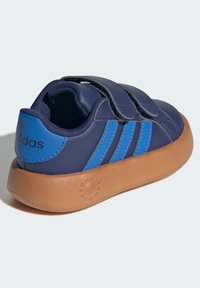 Baskets bleu marine avec deux bandes Velcro, trois rayures bleues sur le côté et une semelle en caoutchouc marron. Présente un col rembourré et une surface texturée.