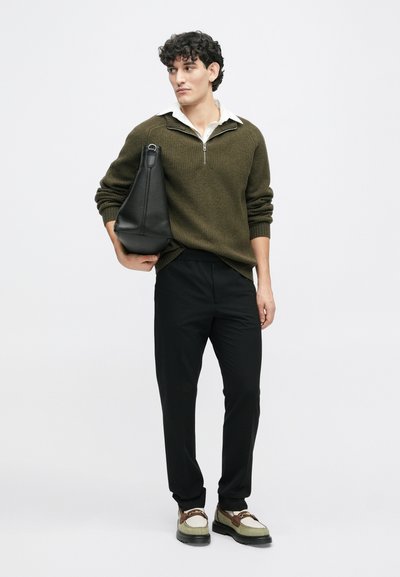 Žalias raukšlėtas megztinis su baltu marškinėlių apykaklė po juo, juodos kelnės ir juoda rankinė. Batai yra daugiakampiai su masyviu padu.