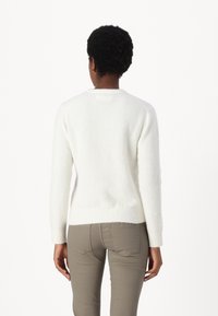 Vit, fluffig tröja med rund halsringning och långa ärmar, med en ribbad nederkant. Buren med ljusa, tajta byxor.