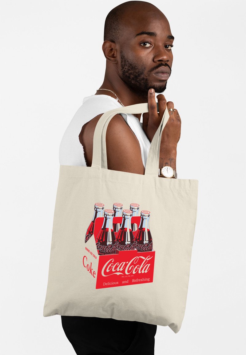 Borsa in cotone beige con una grafica di bottiglie di Coca-Cola classiche su uno sfondo rosso. Manici spessi, texture liscia e design resistente.