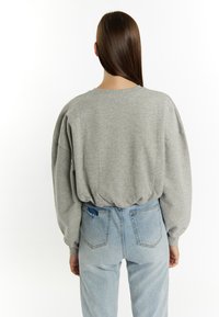 Grijze oversized sweatshirt met een ronde hals en een gathered zoom, gecombineerd met lichtblauwe jeans met een versleten detail op de achterzak.