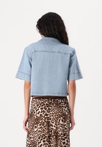 Jaqueta de denim azul claro com mangas curtas e um corte cropped, apresentando bainhas desfeitas e um colarinho clássico. Combinada com uma saia de estampa de leopardo.