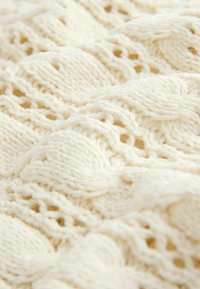 Cream-colored knitted fabric featuring a textured, wave-like pattern with openwork details, showcasing a soft and slightly fuzzy appearance.
