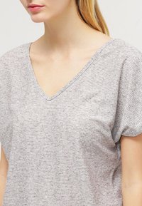 Top gris de manga corta con diseño de escote en V. El material parece suave y ligeramente texturizado con rayas horizontales. Ajuste casual.