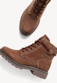 Bottes de cheville en cuir marron à lacets avec des semelles en caoutchouc robustes et des coutures blanches contrastantes, présentées en vue de côté et de dessus sur un fond blanc.