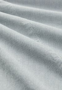 Primo piano di un tessuto grigio chiaro con sottili righe verticali nere e dettagli di cucitura diagonale visibili.