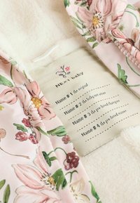 Lilleline beebiriietus pehmest kangast, millel on roosa taust suurte õitega ja kreemjas tekstuuriga vooder; sisaldab nimega silda.