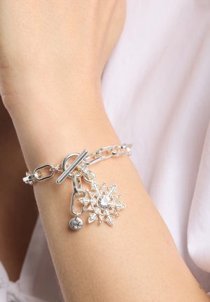 Pulsera de cadena de plata con cierre de toggle, que presenta un charm decorativo en forma de copo de nieve adornado con patrones geométricos y una piedra central.