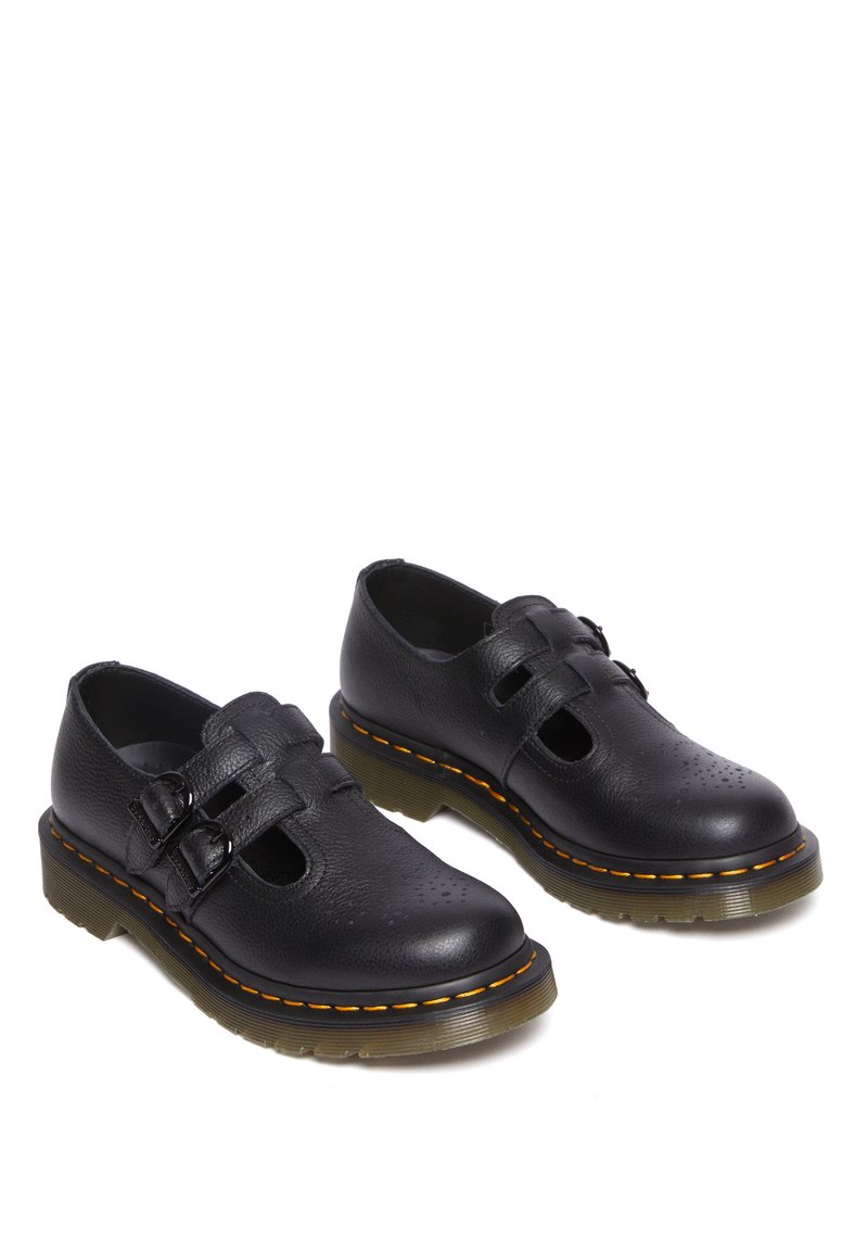 Schwarze Lederschuhe mit zwei Schnallenriemen, perforiertem Design, runder Zehenpartie und einer dicken, klaren Gummisohle mit orangefarbenem Steppdetail.