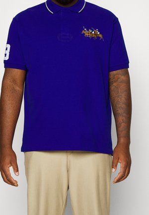 Fioletowa koszulka polo z białym kołnierzykiem i lamówką, z haftowanym motywem konia do polo na piersi oraz cyfrą "3" na rękawie.