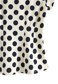 Marineblåt polkaprikket mønster på en cremefarvet stof. Korte ærmer, tætsiddende form og en buet kant. Synlige sømme langs kanterne.