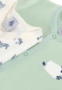 Hellgrüner Baumwoll-Body mit einer weißen Schaf-Applikation. In der Nähe befindet sich ein kremfarbener Body mit navyblauen Tiermustern und kontrastierenden grünen Druckknöpfen.
