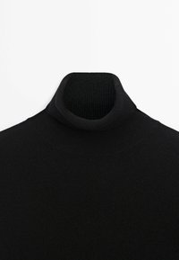 Pull à col roulé côtelé noir avec col replié, présenté sur un fond blanc.