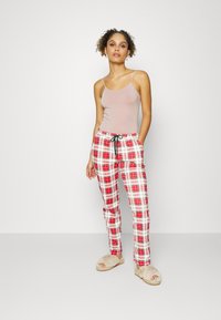 Calças de pijama em padrão xadrez vermelho e branco, com uma cintura elástica e cordão preto, combinadas com uma t-shirt leve e pantufas felpudas bege.