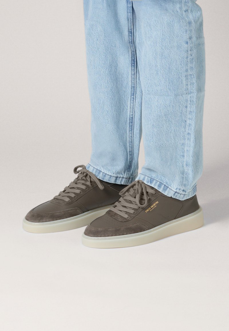 Grijze suède en leren sneakers met een gladde zool, voorzien van beige accenten en tonale veters. Gouden branding op de zijkant voegt detail toe.