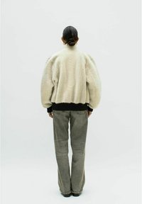 Faux-Fur-Jacke in Off-White mit runder Silhouette, geripptem schwarzen Bund und langen Ärmeln, kombiniert mit grauen weiten Jeans.