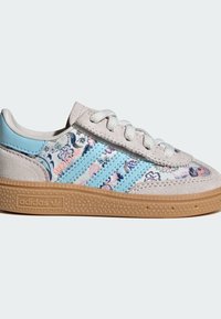 Baskets basses Adidas en daim beige, avec des rayures bleues, un tissu à motif floral, des lacets blancs et une semelle texturée marron clair.