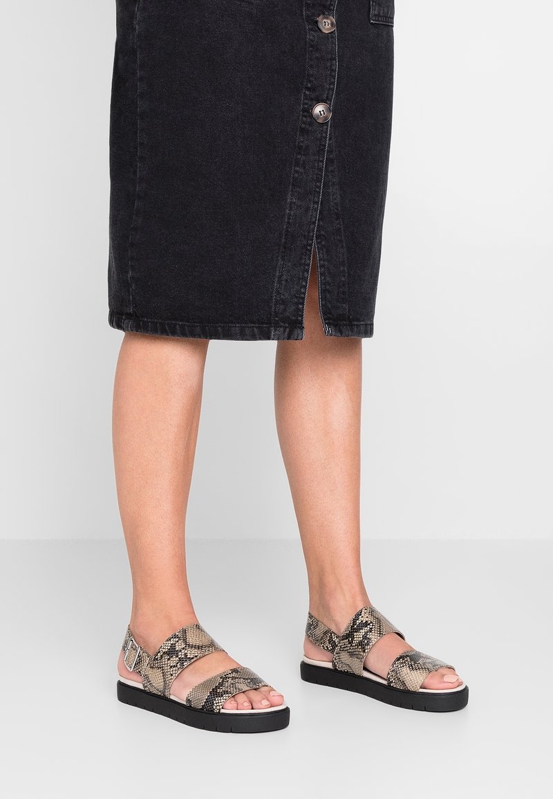 Tas sandalias rata-rata dengan desain cetakan ular, dilengkapi dengan dua tali lebar dan sol hitam. Tali tersebut terbuat dari material dengan tekstur.