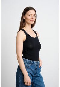 Czarny top na ramiączkach wykonany z elastycznej tkaniny z okrągłym dekoltem, zestawiony z wysokim stanem niebieskich jeansów; gładka faktura i dopasowany krój.