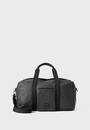 Sac de sport noir en matériau durable avec deux anses supérieures, une bande réglable pour l'épaule et une poche zippée à l'avant. Détails du logo inclus.