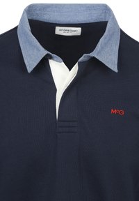 Marineblaues Poloshirt mit einem hellblauen Kragen und weißer Blende, ausgestattet mit einem roten gestickten "MΓG"-Logo und einem strukturierten Stoff mit drei horizontalen Streifen.