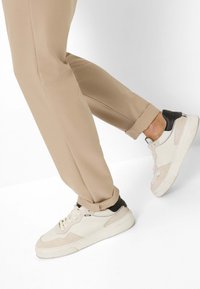 Beige broeken met een gladde textuur, gecombineerd met witte en grijze sneakers met zwarte accenten en een gelaagd ontwerp.