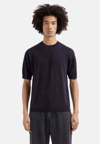 Marineblauwe short-sleeve trui gemaakt van zacht breiwerk, met een ronde hals en een relaxte pasvorm, gedragen met grijze denimbroek.