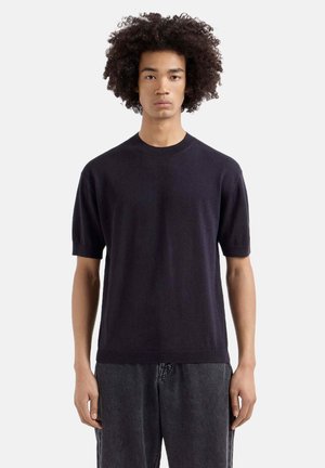 Marineblauer kurzärmeliger Pullover aus weichem Strickgewebe, mit Rundhalsausschnitt und entspannter Passform, kombiniert mit grauen Jeanshosen.