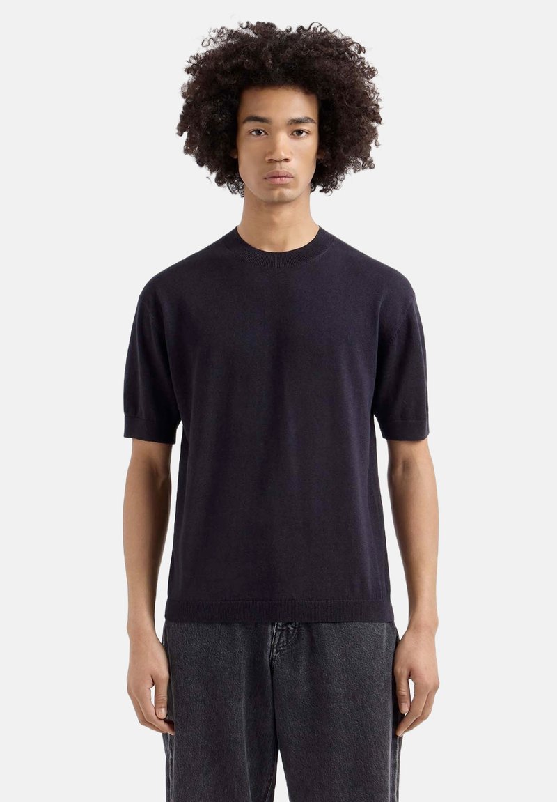 Marineblauwe short-sleeve trui gemaakt van zacht breiwerk, met een ronde hals en een relaxte pasvorm, gedragen met grijze denimbroek.