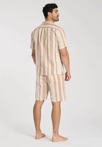 Heren beige set met korte mouwen en korte broek, voorzien van een abstract geometrisch patroon in roest en lichtbruin. Gemaakt van lichte stof.