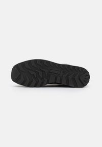 Semelle de chaussure en caoutchouc noir avec un motif en zigzag texturé pour une adhérence et une durabilité, présentant un design robuste et intrépide.
