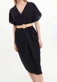 Schwarzes Leinenkleid mit V-Ausschnitt, kurzen Ärmeln und einer taillierten Taille, die durch einen gewebten beigen Gürtel mit runder Schnalle betont wird. Mittellanges Design.