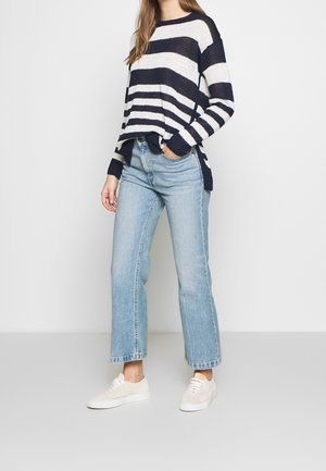 Marineblå og hvide stribede strikketrøje, afslappet pasform, sideslids, parret med lyseblå højtaljede jeans og beige sneakers.