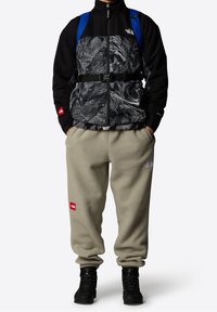 Svart och gråmönstrad jacka med hög krage, beige fleecebyxor och svarta stövlar, med logotyp på jackan och byxorna.