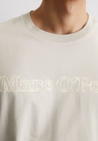 Lichtbeige katoenen t-shirt met reliëftekst "Marc O'Polo" in een gestileerd lettertype over de borst, met een klassieke ronde hals.